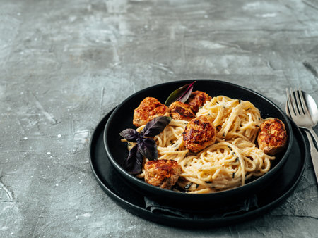 Meatballs Pasta Carbonara in black craft plate over gray background. Close up view of creamy carbonara pasta with meatballs with copy space. Comfort food conceptの写真素材