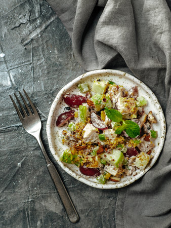 Waldorf salad, copy space. American fruit and nut salad with apples, celery, grapes, chicken meat, dressed mayonnaise. Craft plate with ready-to-eat waldorf salad on gray background.Top view. Verticalの写真素材