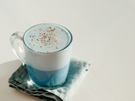 Blue pea latte or blue matcha latte with copy space. Hot fresh milk with blue butterfly pea flowers or clitoria ternatea latte in glass cup at natural sunset hard light. White backgroundの写真素材