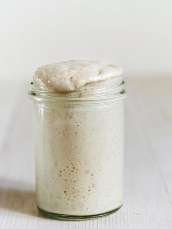Wheat sourdough starter. Glass jar with sourdough starter on white wooden tabletop. Copy space for text or design. Vertical.の写真素材