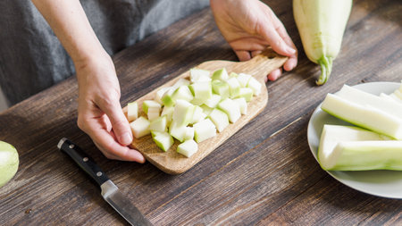 Zucchini harvest. Woman slices zucchini cubes for freezing on wooden table. Zucchini Cooking and Diet Meal Conceptの写真素材