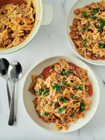 Pasta Farfalle with tomato sauce and ground meat in plate on white marble tabletop. Idea and recipes for easy, simple lunch or dinner one-pot meat goulash. Top down view or flat lay. Verticalの写真素材