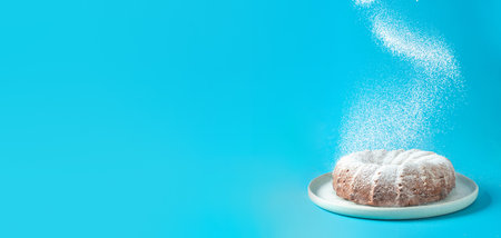 Icing sugar falling of fresh home made bundt cake. Powder sugar falls on fresh bunt cake over blue background. Copy space for text. Ideas and recipes for breakfast or dessert. Bannerの写真素材