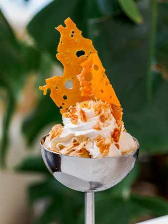 Two flavors of ice cream - coffee ice cream and butter icecream topped with whipped cream, caramelized almonds, decorated crunchy caramel. Delicious ice cream in metal sundae bowl on tableの写真素材