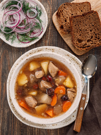 Clear soup with pork, potato, carrot and rosehip. Traditional russian siberian baikal soup yushka with meat. Perfect authentic delicious clear broth soup in rustic style on brown wooden background.の写真素材