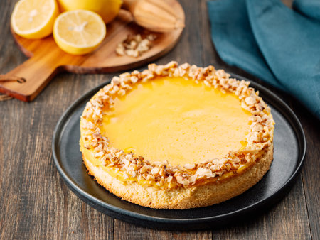 Vegan lemon tart or lemon cake, modernly decorated chopped walnuts. Delicious whole lemon pie on plate on wooden background. Aesthetic of traditional classic french yellow tart with lemon curd recipeの写真素材