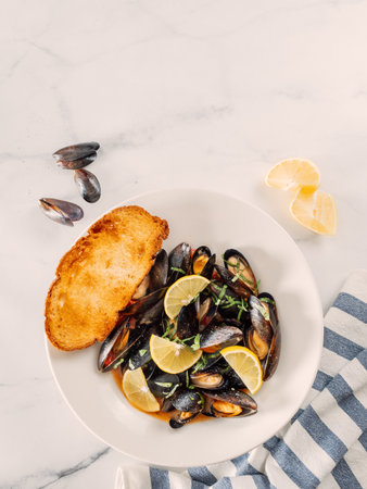 cooked mussels with lemon on white plate. Restaurant-style seafood plating. Seafood and mossels food background. Top view, copy space, verticalの写真素材