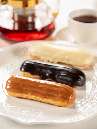 Group of french dessert Eclair on white plate. Caramel, chocolate and vanilla glazed eclairs on white plate in restaurant table background. Perfect french eclairs setの写真素材