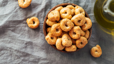 Traditional italian snack taralli or tarallini in wooden bowl over gray linen napkin background. Rustic shot of taralli appetizer with copy space. Top view or flat lay. Horizontal bannerの写真素材