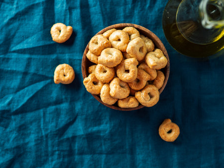 Traditional italian snack taralli or tarallini in wooden bowl over dark blue linen napkin background. Rustic shot of taralli appetizer with copy space. Top view or flat lay.の写真素材