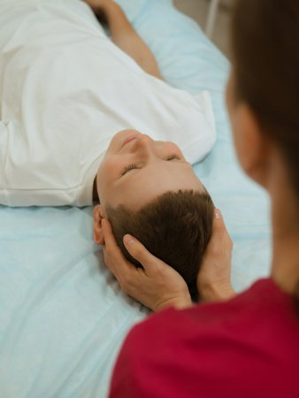 Osteopathy Treatment. Boys head being manipulated by real osteopathic physician. Naturopath treats kid with osteopathy as alternative medicine and therapy. Osteopath harmonizes bodyの写真素材