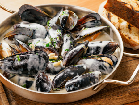 Delicious black mussels in creamy cheese and garlic sauce. Mediterranean black mussels in metal pan on wooden cutting board with grilled bread on wooden backgroundの写真素材