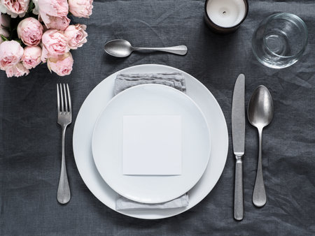Menu, wedding invitation mock up. Beautiful table setting on gray linen tablecloth. Festive table setting for wedding dinner with pink spray roses and cabdle. Holiday dinner, white plates. Copy spaceの写真素材