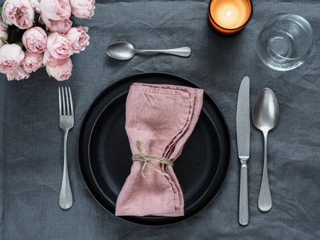 Beautiful table setting with pink spray roses and candle on gray linen tablecloth. Festive table...