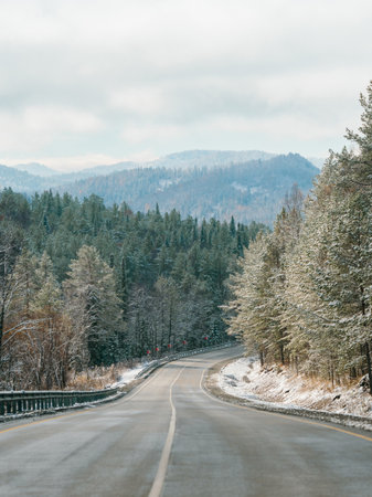Winter road in snowy mountains. Autumn or wintertime in mountains. Asphalted road through fir tree...