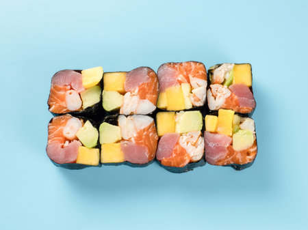 Top view of roll with mango, avocado, shrimp, salmon and tuna. Studio photography of colorful maki roll with shrimp, salmon and tuna. Isolated on solid light blue background.の写真素材