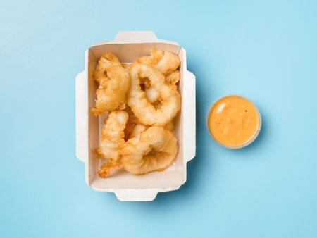 Oven baked breaded calamari or Kara-age squid rings served with sweet and sour sauce. Top view or flat lay. Isolated on blue solid background. Crispy Delight Tangy, Tempting. The Perfect Karaage Squidの写真素材