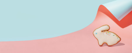 Easter bunny cookie on pink and blue curved paper pastel background with shadows. Happy Easter Day concept. Minimal Easter concept. Copy space for text. Easter cooking baking background.の写真素材