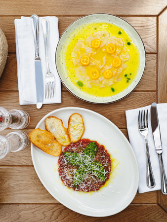 Fresh sea bream carpaccio with salad and tuna or beef tartar with pesto sauce and parmesan cheese. Two types of antipasti appetizers on wooden table, top view or flat layの写真素材