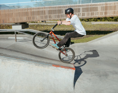 Skilled BMX rider performing Manual trick in ramp park. Young BMX bicycle rider having fun and posing in Manual Wheelie riding outdoors. Riding in back wheel in street park. Concrete street parkの写真素材
