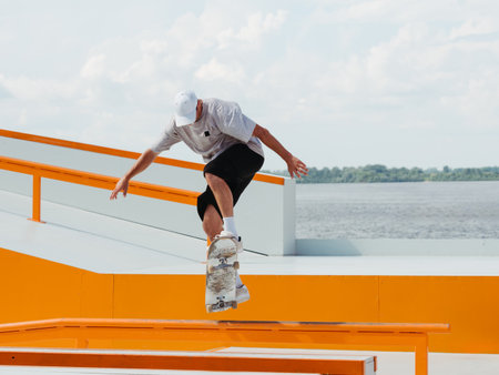 Caucasian Boy doing jump trick through rail on skateboard in skatepark. Professional sportsman jumping and doing trick on skateboard in outdoor parkの写真素材