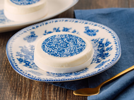 Pastry dessert in Gzhel rustic style. Sweet pastry decorated blue flowers photo printing on sugar paper. Mini cake Gzhel on plate over wooden tabletop background. Closeupの写真素材