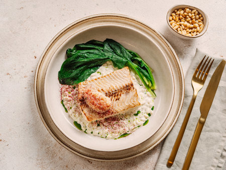 White fish on pillow of pine nut garnished with blanched spinach and caviar, on restaurant table. Delicious dish with whitefish, top viewの写真素材