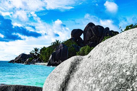 monolith of granite in the foreground blocks the gaze of a paradisiacal beach in the Seychelles with a crystal clear sea and a blue skyの写真素材