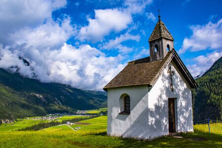 Alpine church surrounded by green meadows and very high mountains in the otztal valley in the Austrian Alps of Tyrol on a cloudy summer dayの写真素材