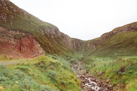 tumultuous stream descends downstream between two green Scottish hills