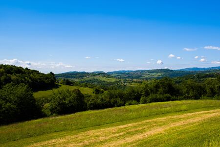 green agricultural fields on the hills in the foreground with sky and plain in the backgroundの写真素材