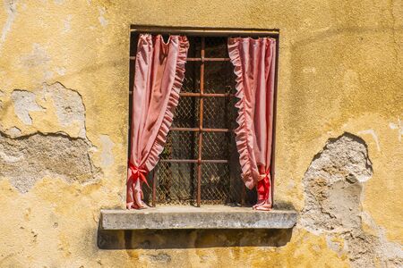 window with rusty railing and red curtains on old yellow wall peeling from timeの写真素材