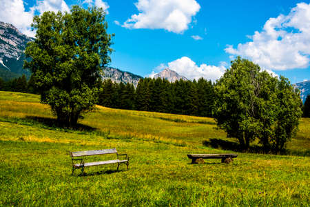 two empty benches one old and one modern in the green pastures around Cortina D'Ampezzo in Belluno, Italyの写真素材
