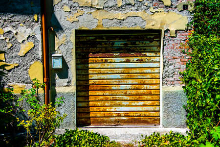 old closed and rusty garage shutter on old house walls in Citerna, Perugia, Umbria, Italy, on a sunny august dayの写真素材