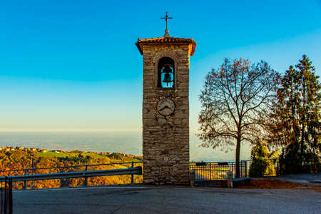 Bell tower in Campana on an autumn day with trees colored red and yellow in Lusiana, Vicenza, Italy