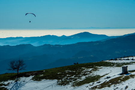 paraglider soars over the snow covered peaks in the pre-Alps above Valdagno, Vicenza, Italyの写真素材