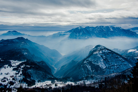 alpine landscape with snowy peaks and misty valleys, with menacing sky snow mountain peaks and blue...