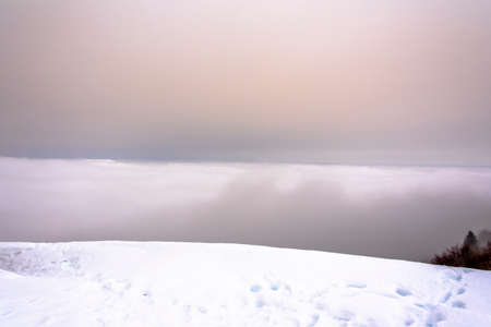 horizon of the Venetian plain immersed in clouds between fog and snow with snowy trees and snowy Alpine peaks on a winter day in Recoaro Mille, Vicenza, Italyの写真素材