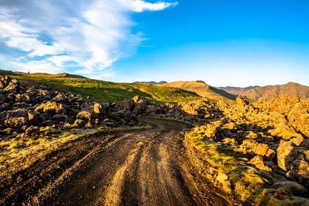 endless lava field crossed by a gravel road at dawn with the ocean in the background in the...