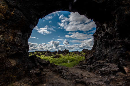 white clouds on blue sky seen through a lava rock arch on Lake Mivatn near Husavik in Nordurping municipality in Icelandの写真素材