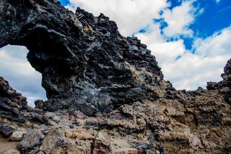 white clouds on blue sky seen through a lava rock arch on Lake Mivatn near Husavik in Nordurping municipality in Icelandの写真素材