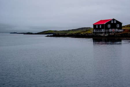 fish factory with red roof and black walls on the shores of Djupivogur harbor in Icelandの写真素材
