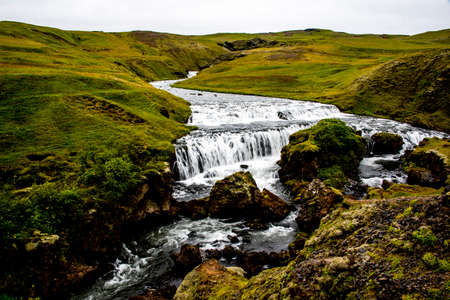 the Skogafoss waterfalls in summer with the green of the mountains and the pouring water near Vik in Icelandの写真素材