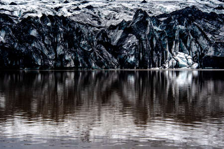 Solheimajokull glacier covered in soot from previous eruptions with the glacial lake descending from...