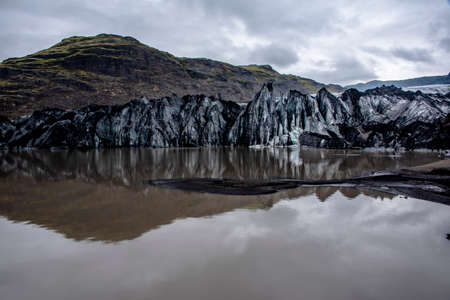 Solheimajokull glacier covered in soot from previous eruptions with the glacial lake descending from the volcano near Vik in Icelandの写真素材