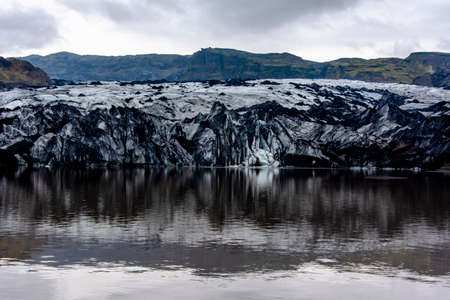 Solheimajokull glacier covered in soot from previous eruptions with the glacial lake descending from the volcano near Vik in Icelandの写真素材