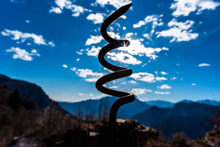 backlight of a rusty iron spiral from time on the blue sky and mountains backgroundの写真素材