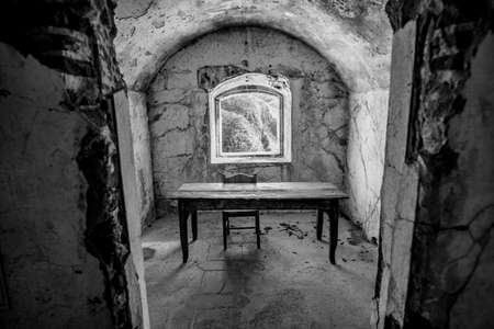 abandoned room of the first world war with old wooden table and chair with window on the rocks of...
