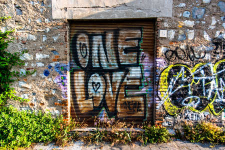 gate with graffiti one love multicolored peeling brick wall with writings near Lake Iseoの写真素材