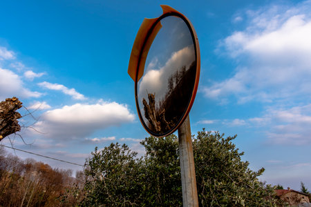 round mirror at the side of the road reflects an old tree and the blue sky in Vallonara Vicenza Veneto Italyの写真素材